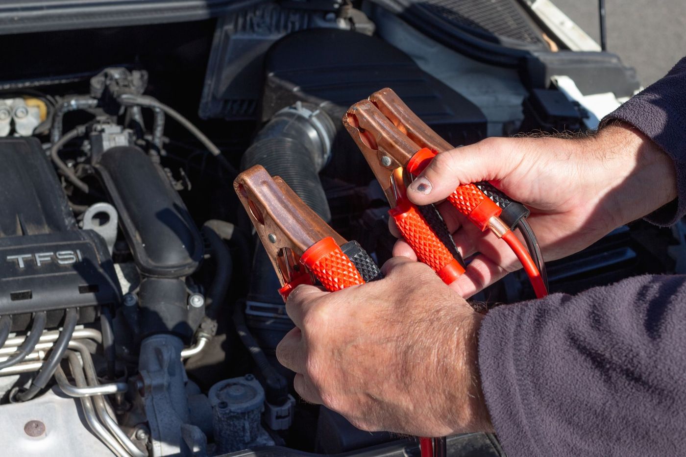 Hands holding jumper cable clamps over an open engine bay — stock photograph