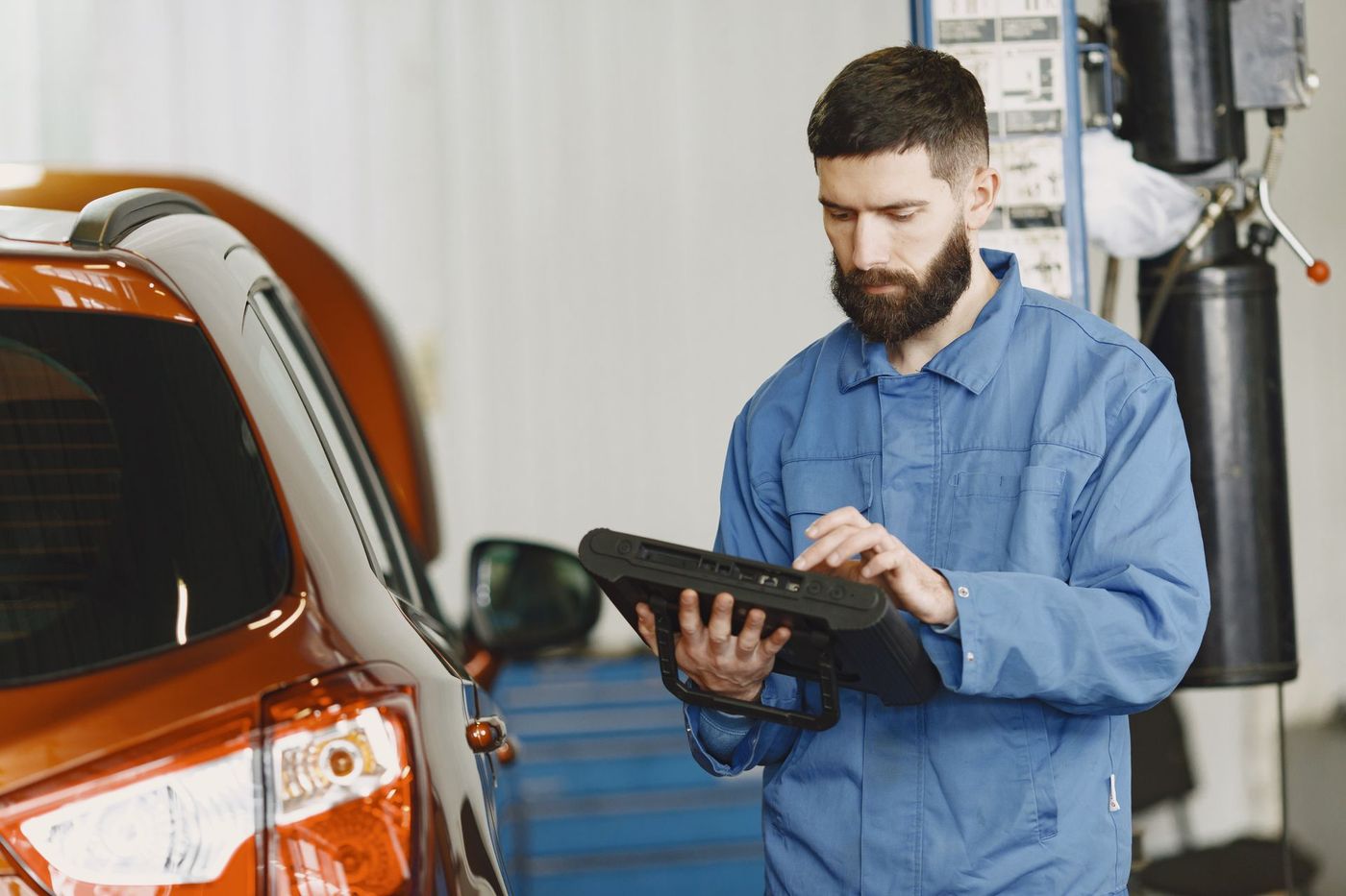 A technician reading a handheld automotive diagnostic tool beside a car — stock photograph