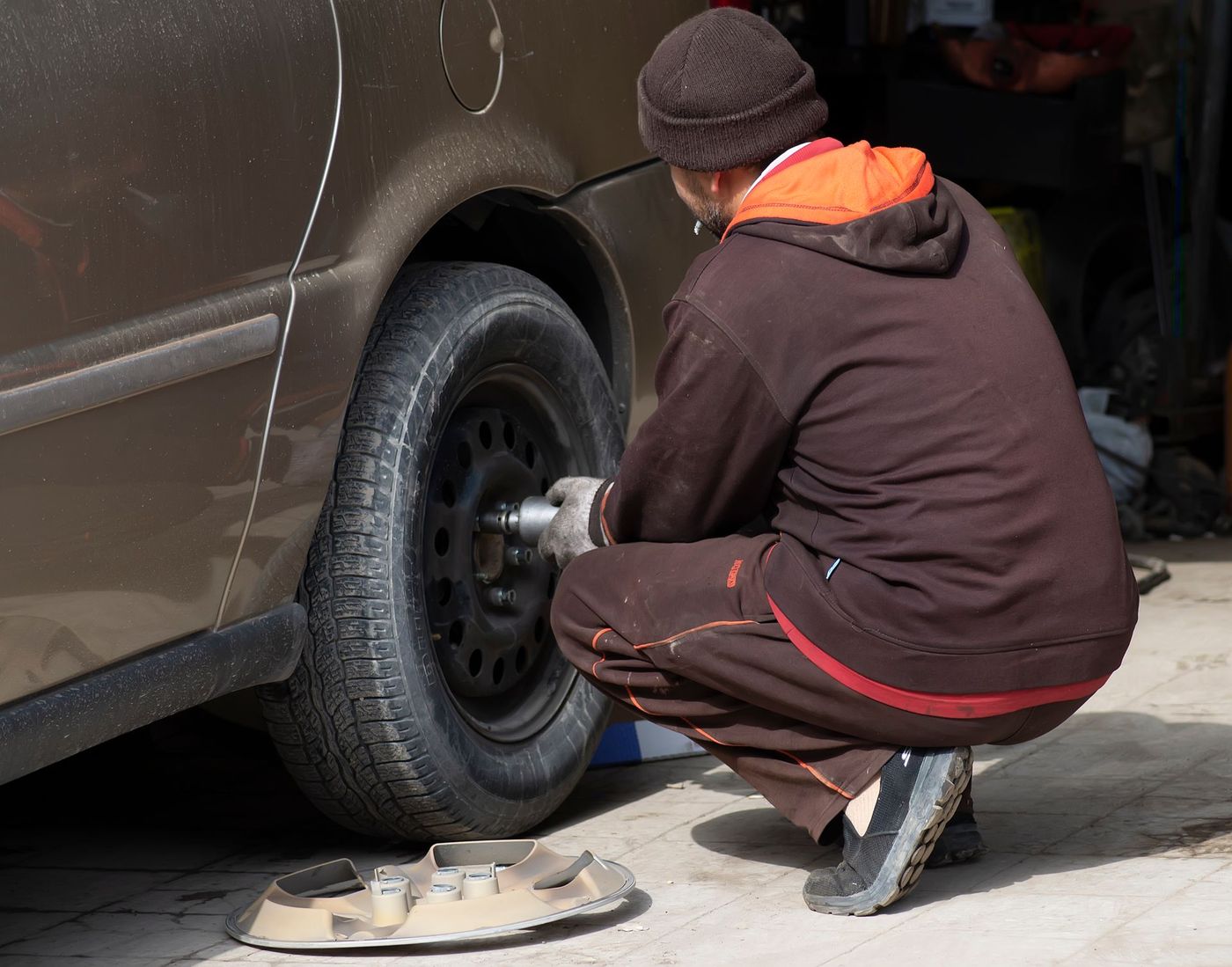 A mechanic using an impact gun on a car wheel in a driveway — stock photograph