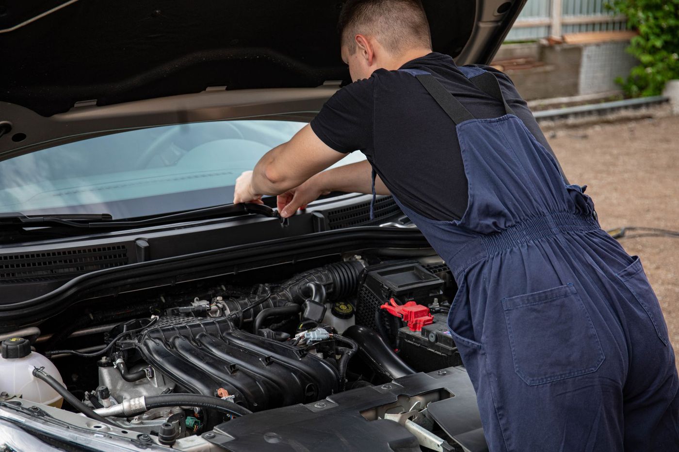 A mechanic leaning into an open hood outdoors on gravel — stock photograph